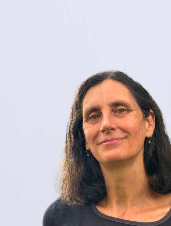 Portrait of Jen Soalt, with a closed-mouth smile, shoulder-length brown hair, a dark grey top, and a blurred white background.