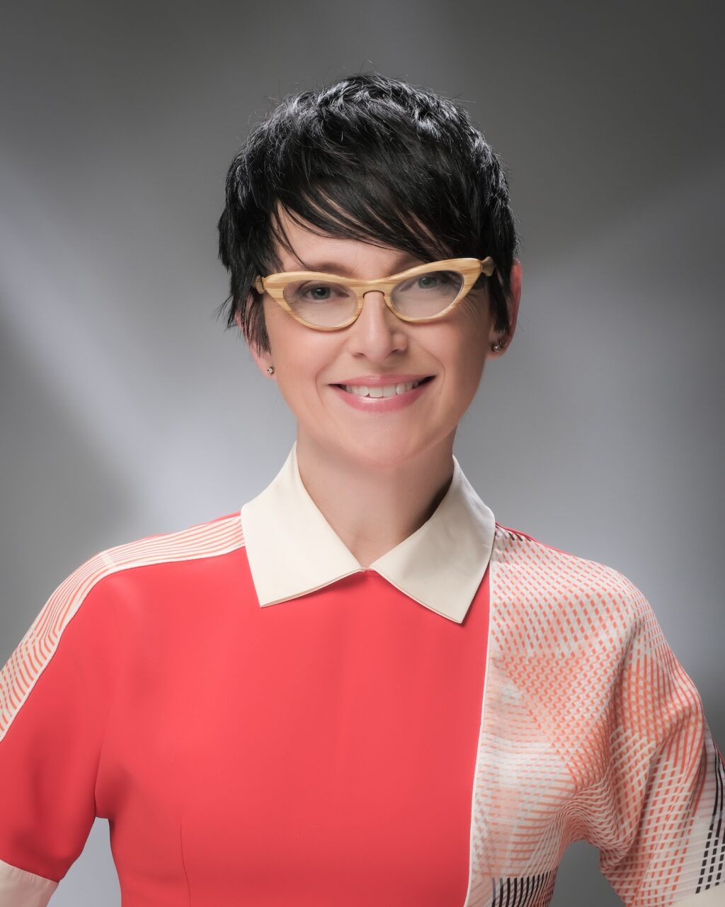 Portrait of competency-based learning expert, Andrea Avery, a smiling woman with short brown hair and glasses, wearing a collared shirt with a white blurred background.